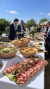 Buffet extérieur avec plats variés sur une nappe blanche, personnes se servant